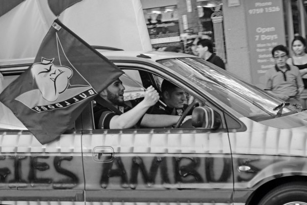 Black and white photograph of Bulldogs fans in a car. The driver is flying a Bulldogs flag out the window as he drives. 