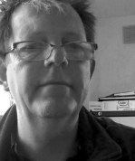 Black and White headshot of Colin Hambrook, a middle-aged, white man wearing glasses
