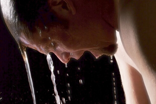 A close up of a man's head, profile looking down with streams of water flowing over his head and face.