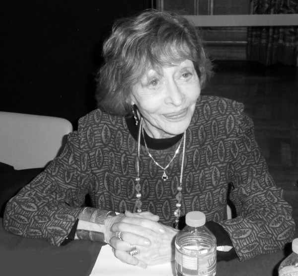 A recent black and white photograph of Alice Cherki, sitting at a table, smiling.