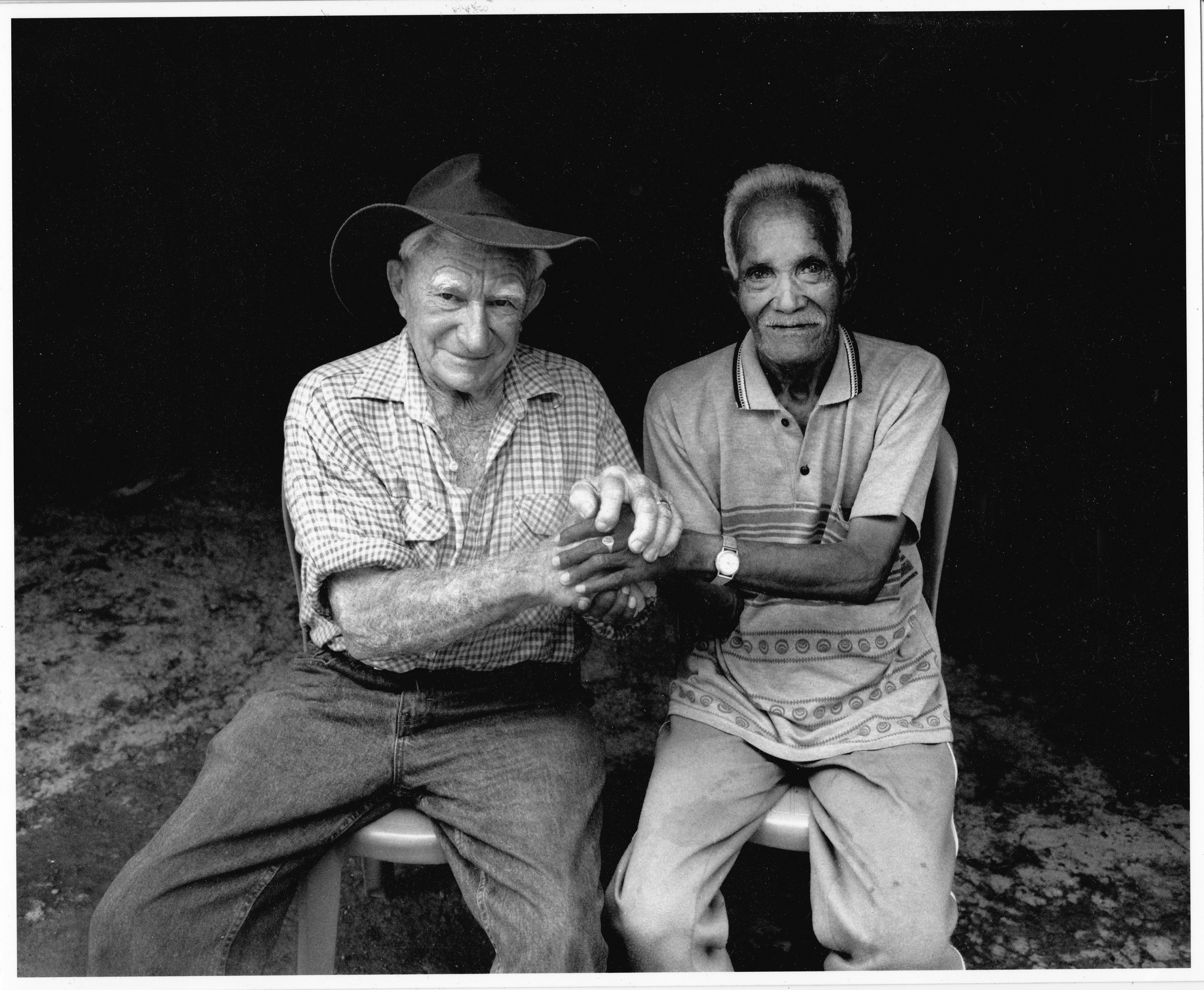 Black and white photograph of World War II veterans, Paddy Keneally and Rufinl Alves seated and holding hands.