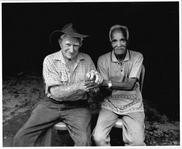 Black and white photograph of World War II veterans, Paddy Keneally and Rufinl Alves seated and holding hands.