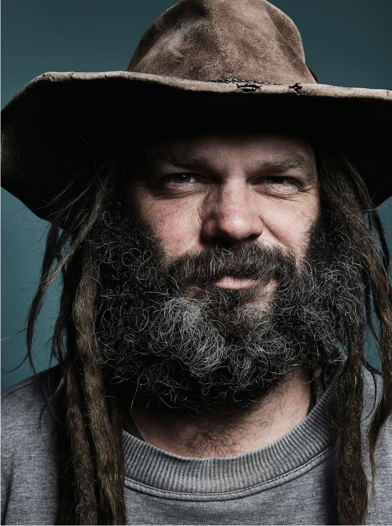 Head shot of Scotty Foster. He has a beard and dreadlocks and is wearing a wide-brimmed, leather hat