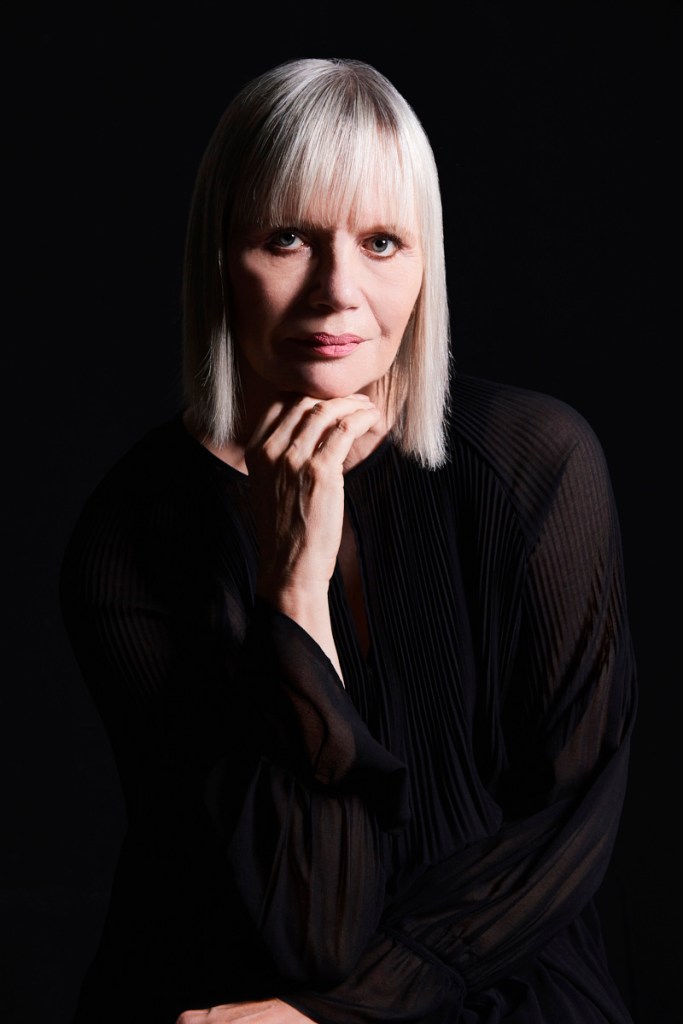Portrait of Gaele Sobott in a dark setting. She is looking at the camera and rests her chin on her hand.